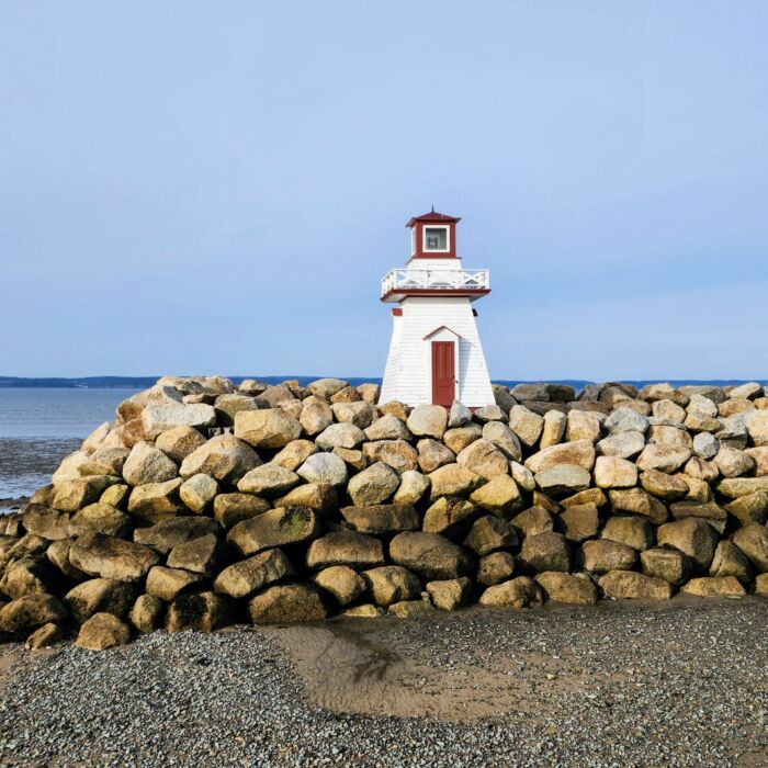 A very small lighthouse sits perched ontop of large rocks along the shoreline.